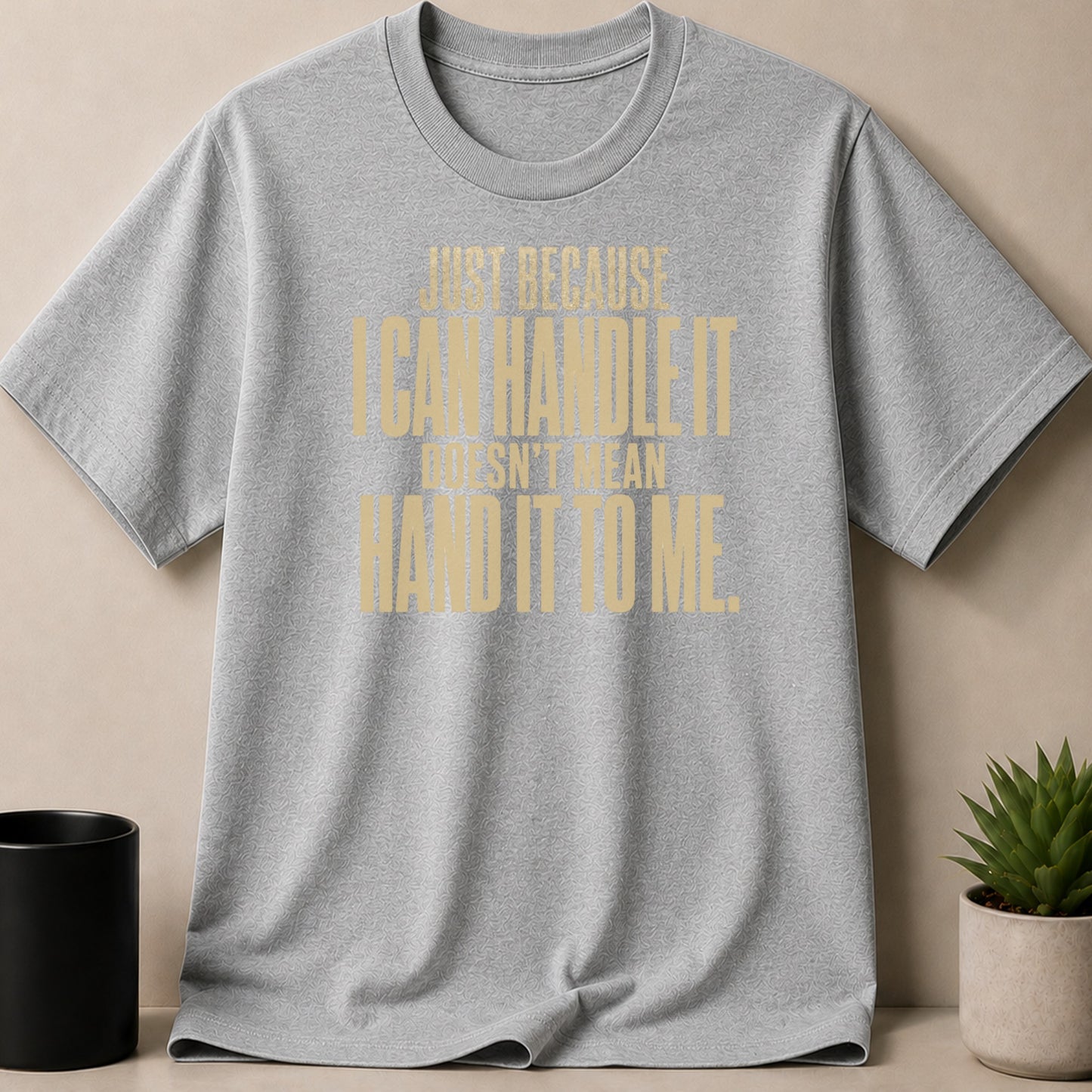Grey t-shirt with gold text reading "Just because I can handle it doesn't mean hand it to me."