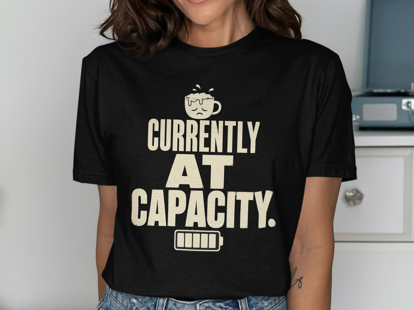 Black t-shirt with text "CURRENTLY AT CAPACITY" and a sad coffee cup and battery.