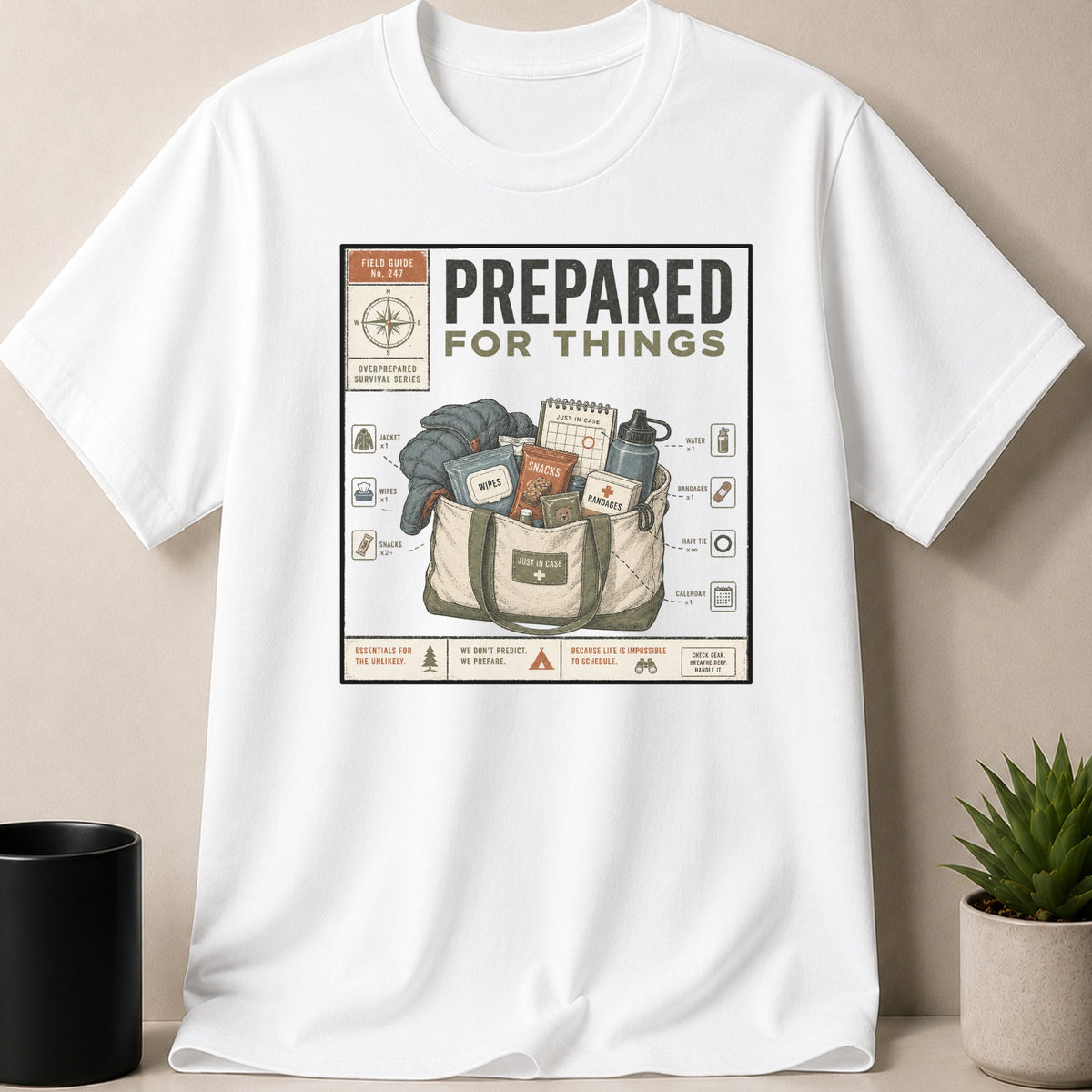 White t-shirt featuring "PREPARED FOR THINGS" with a tote bag and survival items illustration.