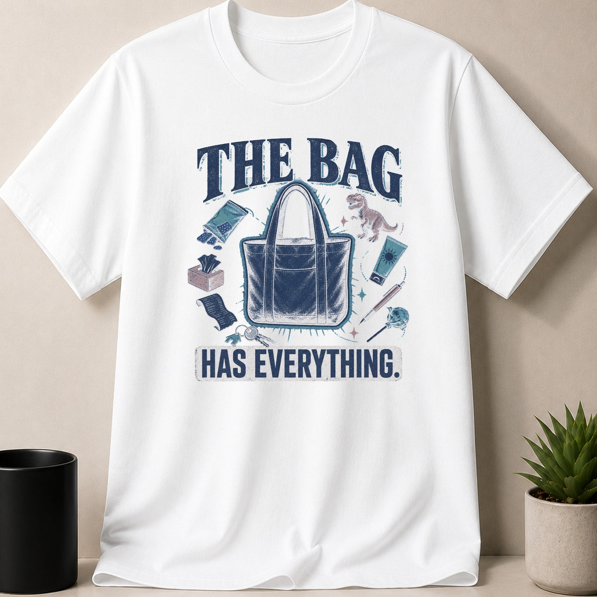 White t-shirt with graphic saying "THE BAG HAS EVERYTHING." and icons of bag contents.