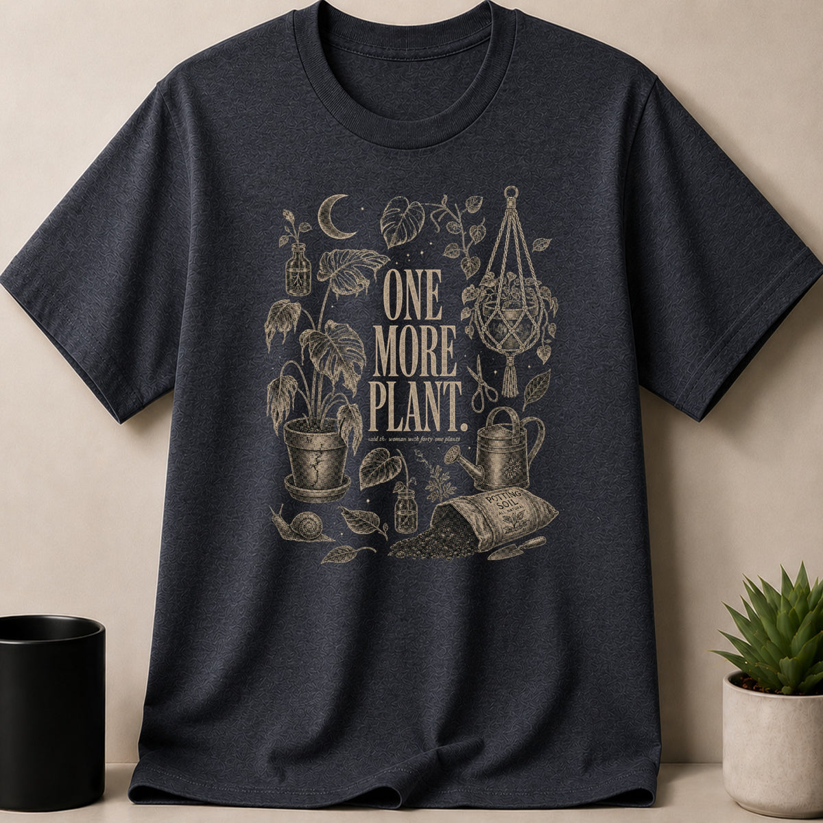 Dark t-shirt with sepia illustration of plants, gardening tools, and text "ONE MORE PLANT."