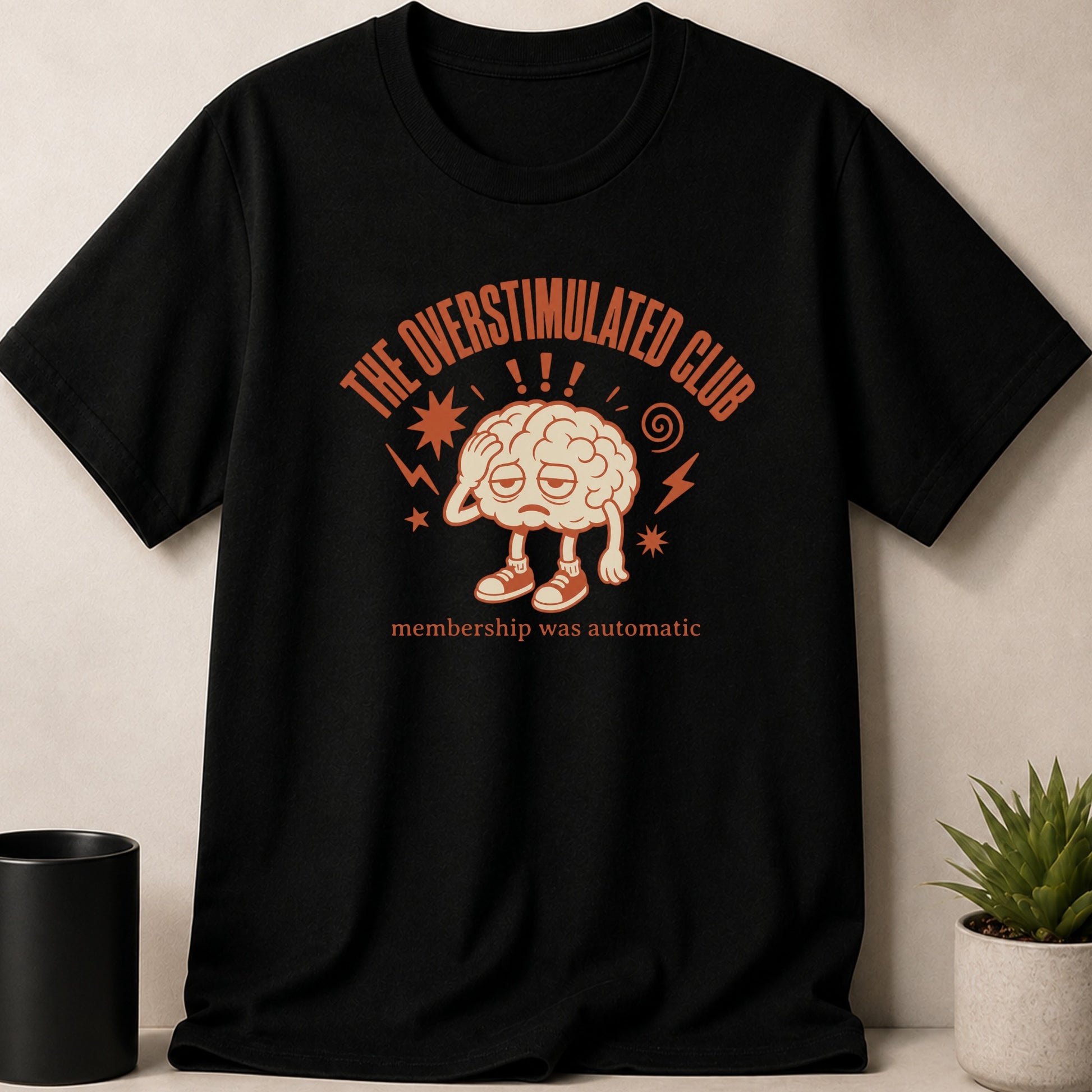 Black t-shirt with "The Overstimulated Club" text and a cartoon brain graphic.