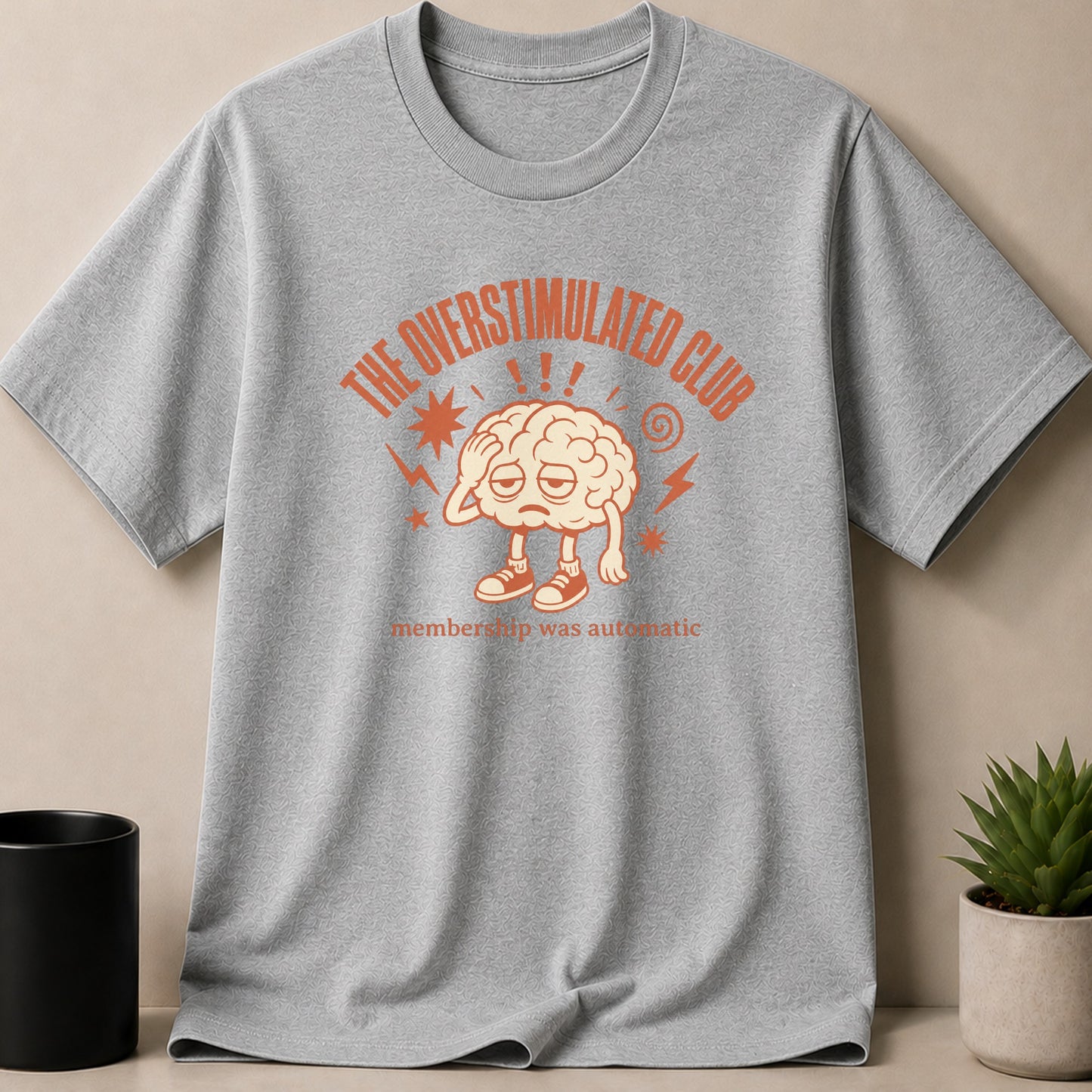Grey t-shirt with "The Overstimulated Club" text and a cartoon brain graphic.