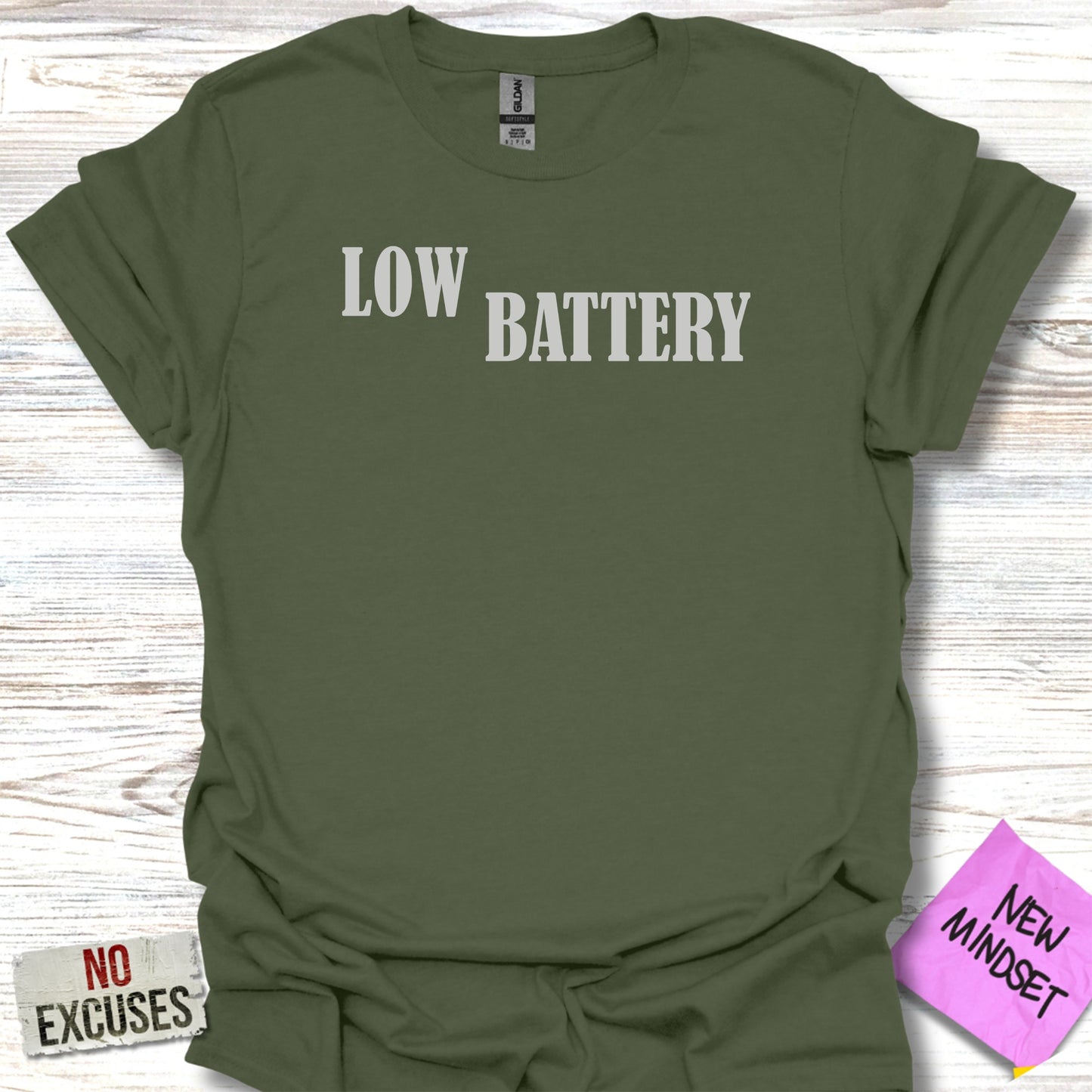Olive green t-shirt with "LOW BATTERY" in white text and "NO EXCUSES" in smaller text.