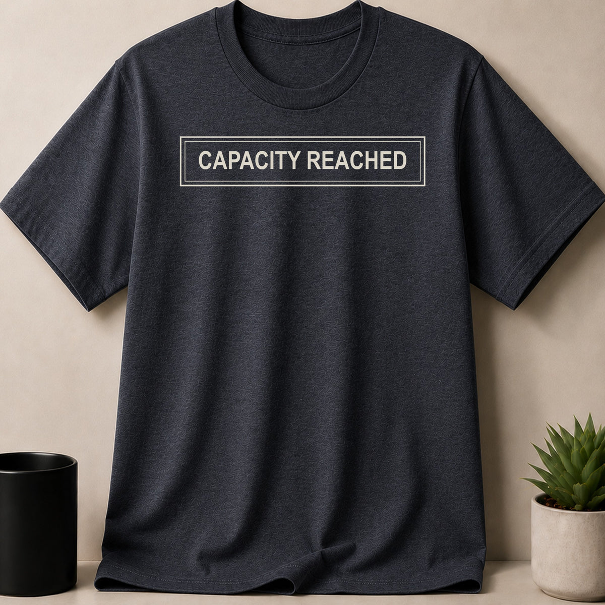 Dark grey t-shirt with white text "CAPACITY REACHED" in a rectangle.