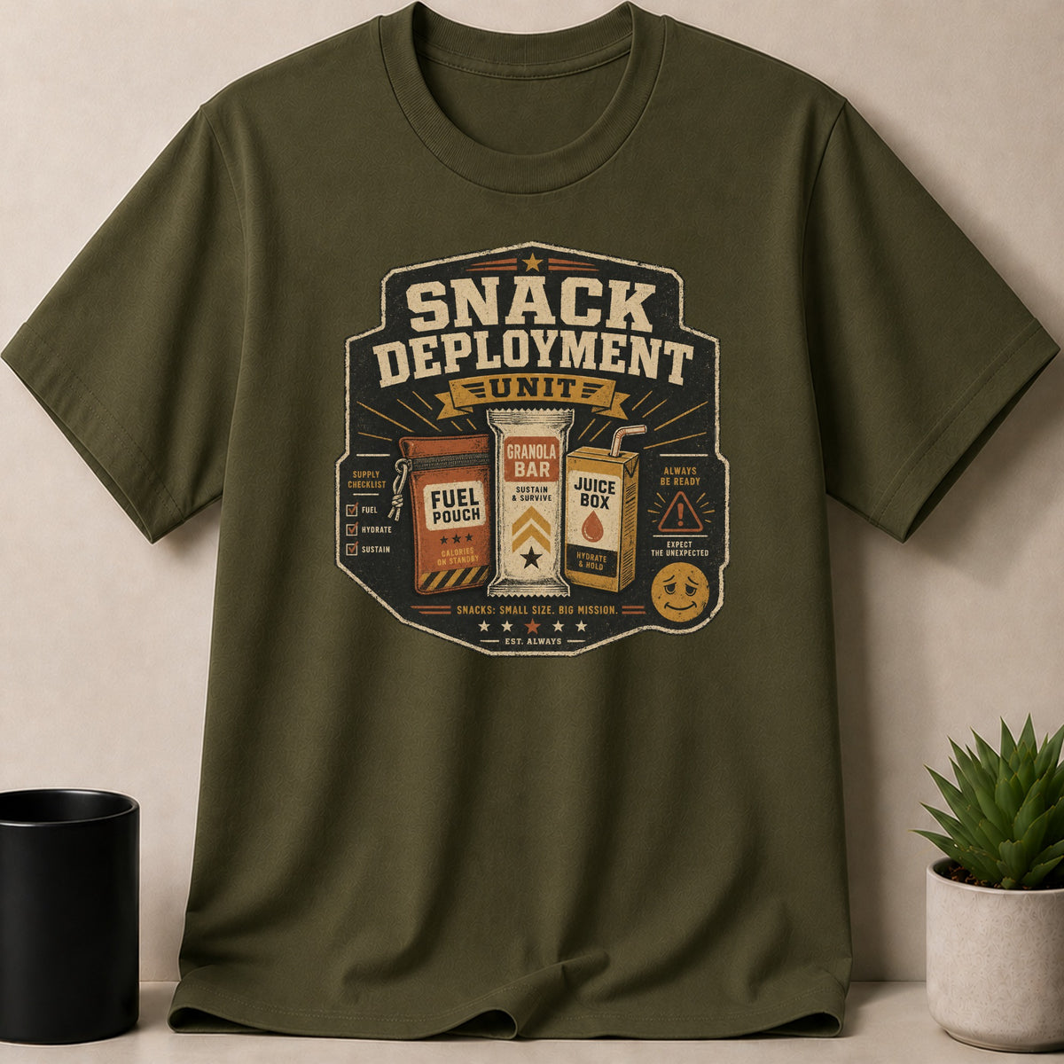 Olive green t-shirt with "Snack Deployment Unit" graphic featuring a fuel pouch, granola bar, and juice box.