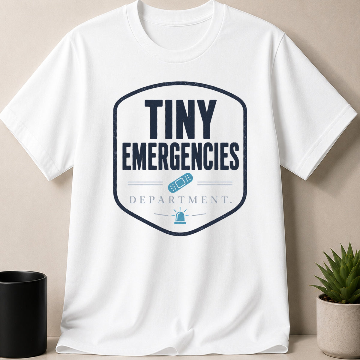 White t-shirt with "Tiny Emergencies Department" text, band-aid, and siren graphic.