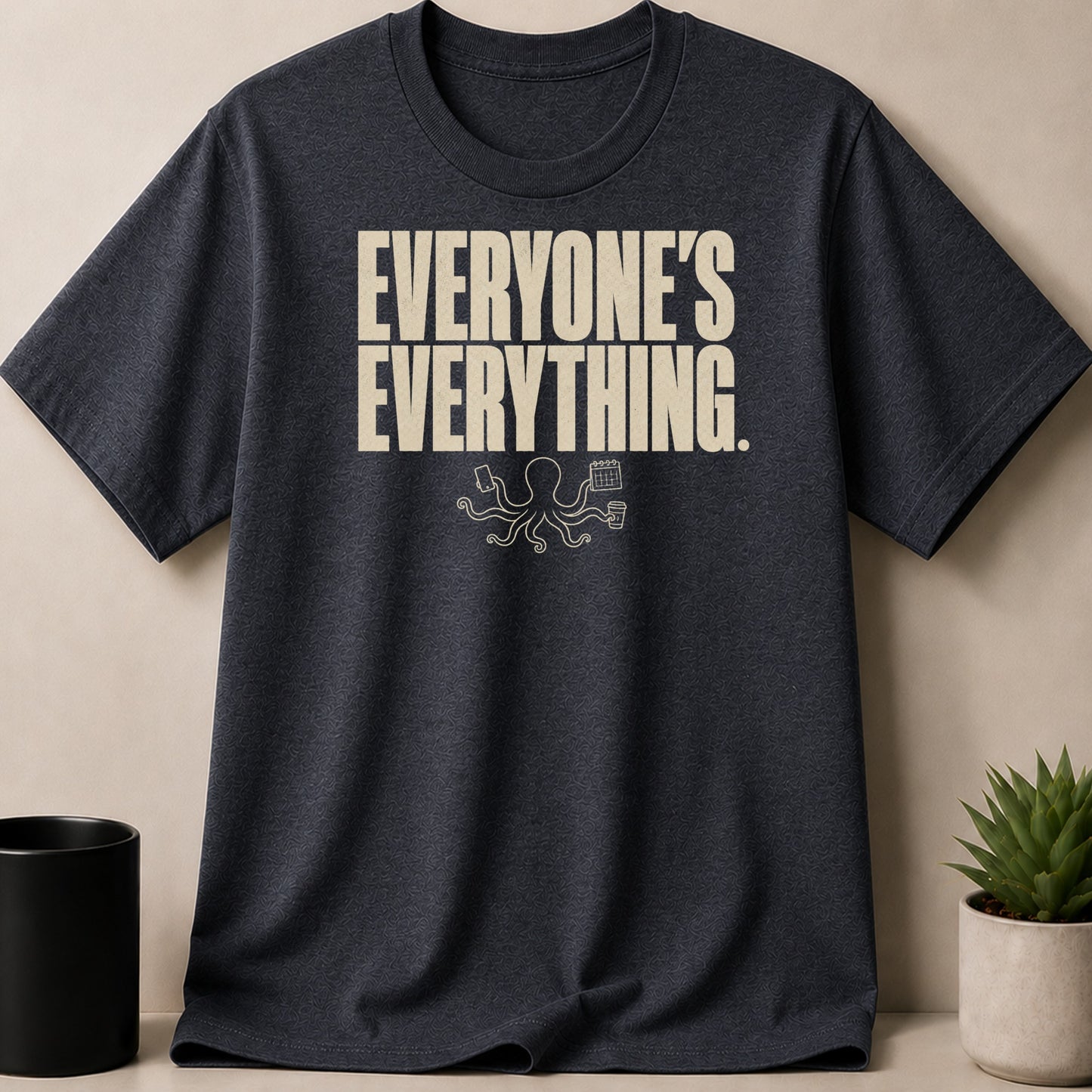 Dark gray t-shirt with "EVERYONE'S EVERYTHING." text and an octopus holding a phone, calendar, and coffee.