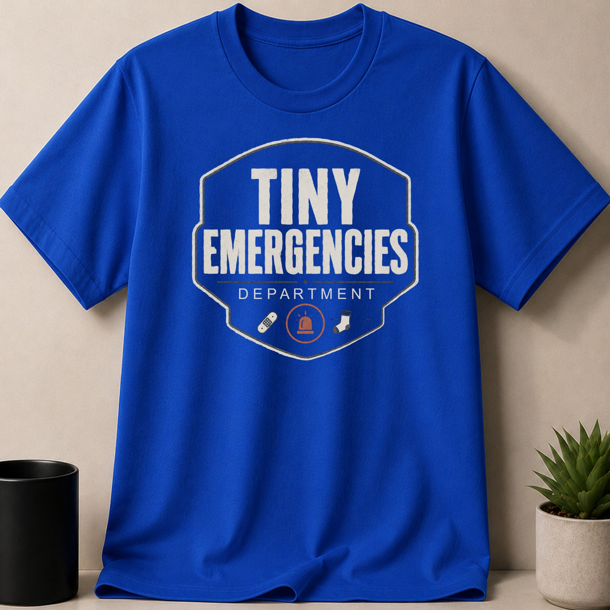 Blue t-shirt with "Tiny Emergencies Department" and icons of a bandage, siren, and sock.