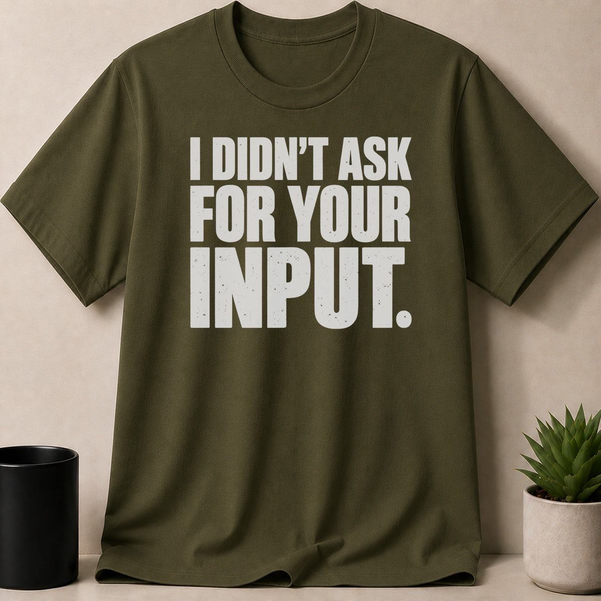 An olive green t-shirt with white block lettering reading I DIDNT ASK FOR YOUR INPUT.