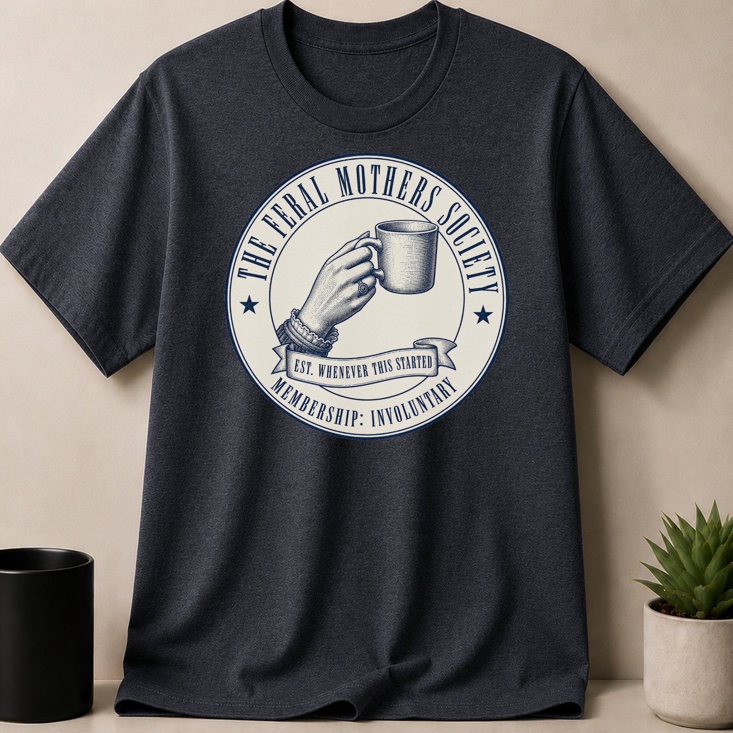 Dark t-shirt with "The Feral Mothers Society" circular graphic featuring a hand holding a mug.