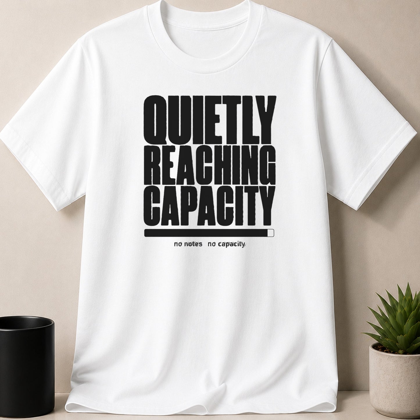 White t-shirt with black text "QUIETLY REACHING CAPACITY" and a progress bar.