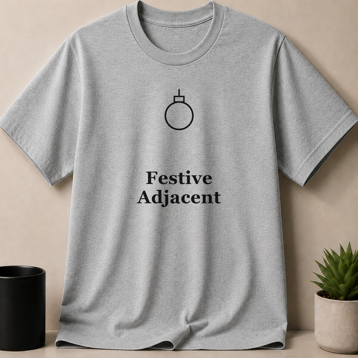 Heather gray short-sleeve t-shirt with a minimalist black holiday ornament graphic and the text Festive Adjacent.