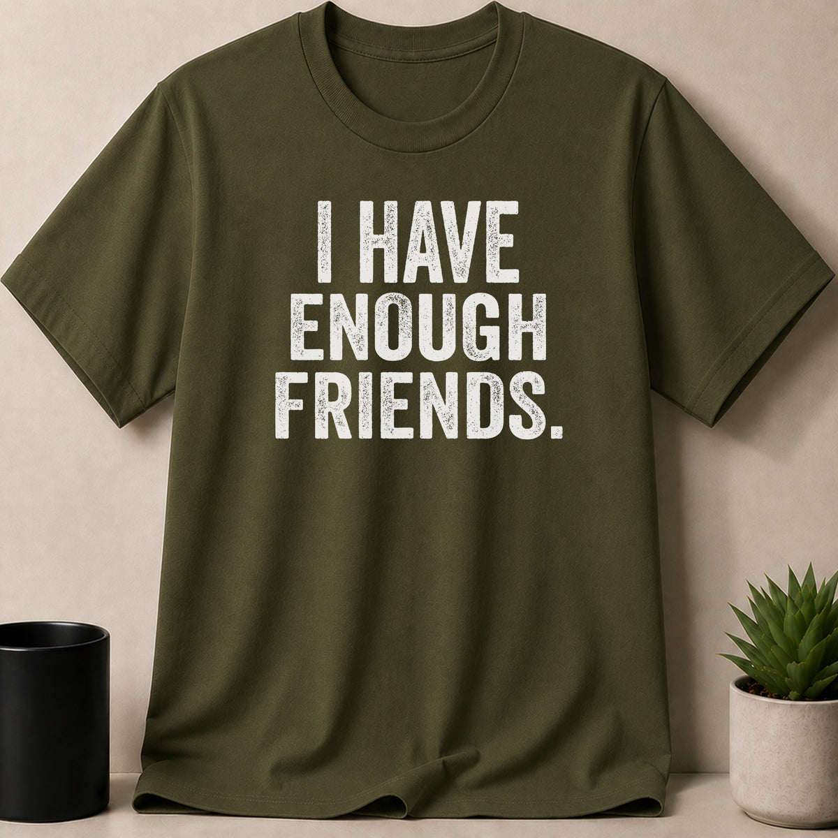 Olive green t-shirt with white distressed text that reads "I HAVE ENOUGH FRIENDS."