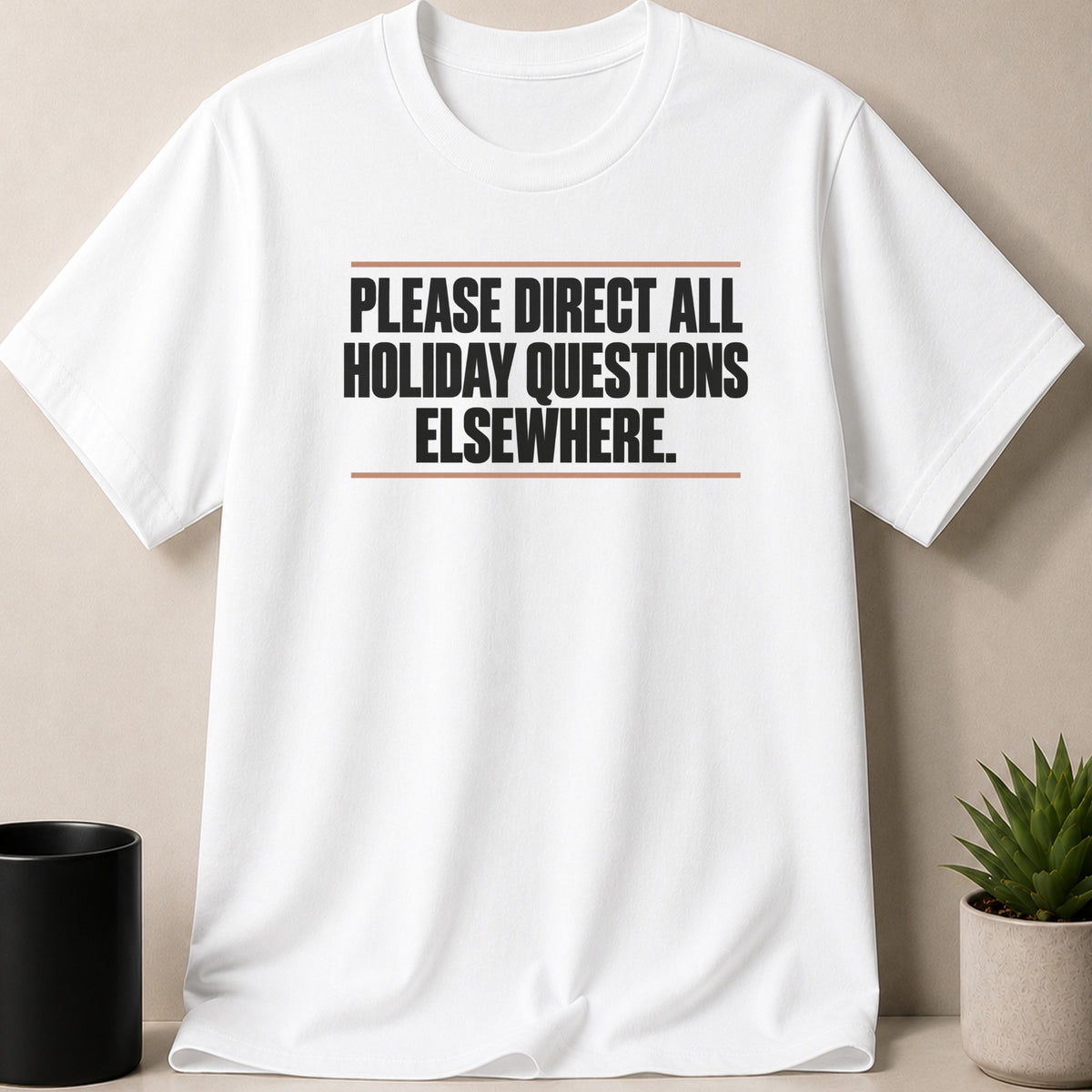 A white short-sleeved t-shirt features black text reading PLEASE DIRECT ALL HOLIDAY QUESTIONS ELSEWHERE between two horizontal brown lines.