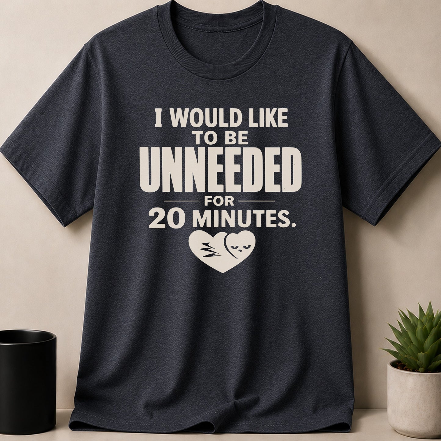 Dark t-shirt with beige graphic saying "I WOULD LIKE TO BE UNNEEDED FOR 20 MINUTES."