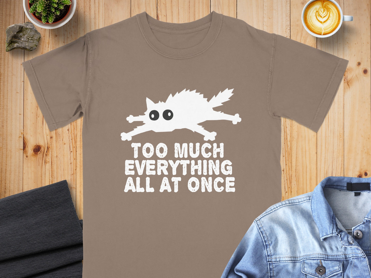 Brown t-shirt with white cartoon cat and text "TOO MUCH EVERYTHING ALL AT ONCE".