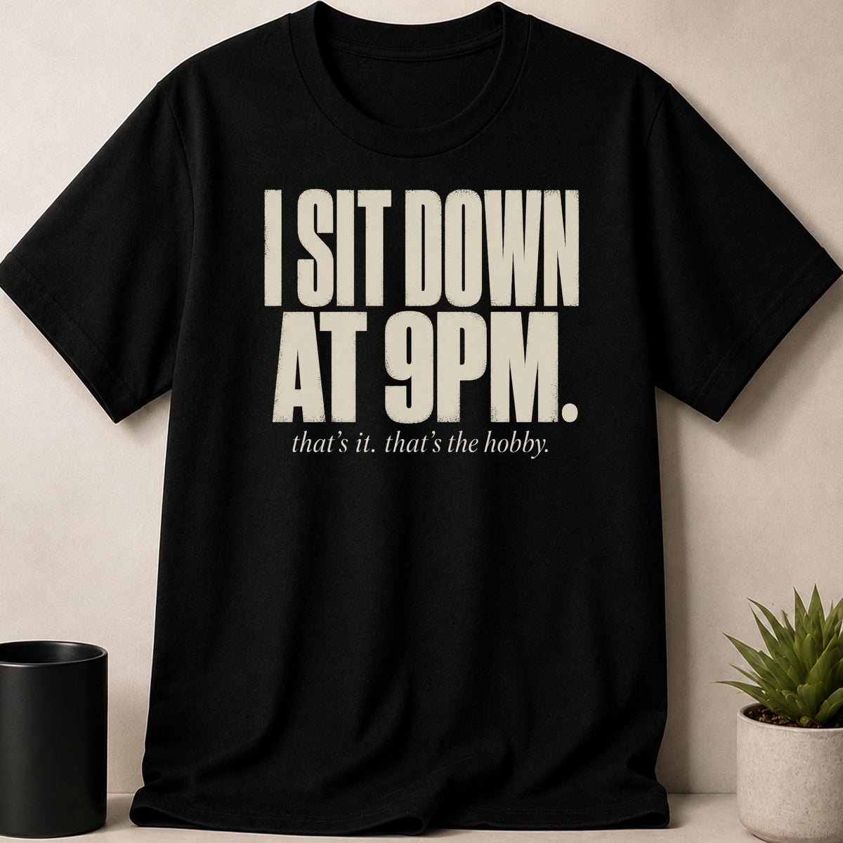 Black t-shirt with cream text "I SIT DOWN AT 9PM. that's it. that's the hobby."