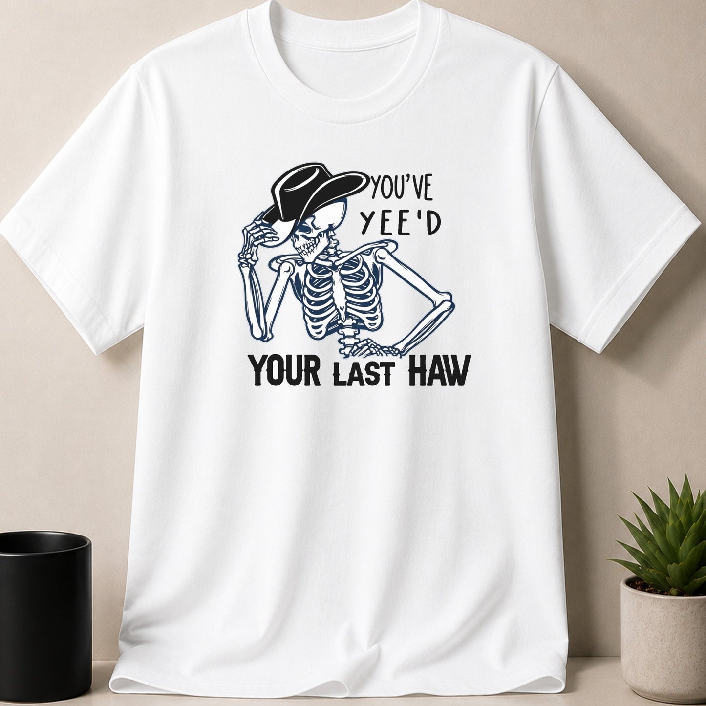 White t-shirt with skeleton wearing a cowboy hat, text reads "YOU'VE YEE'D YOUR LAST HAW".