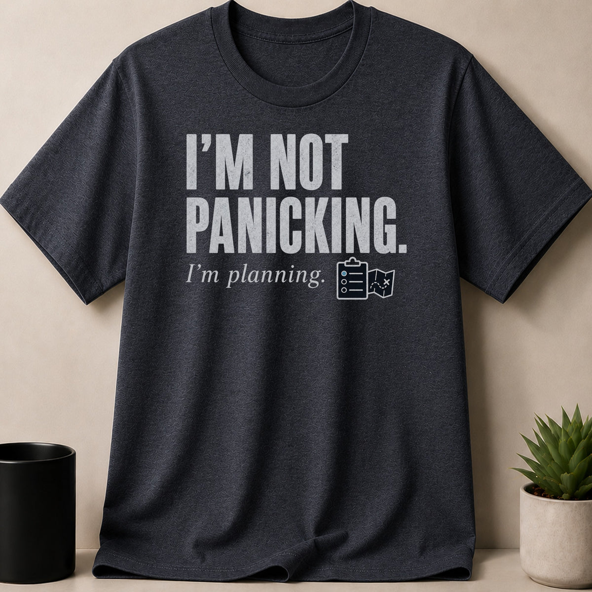 Dark grey t-shirt with white text "I'm not panicking. I'm planning." and planning icons.