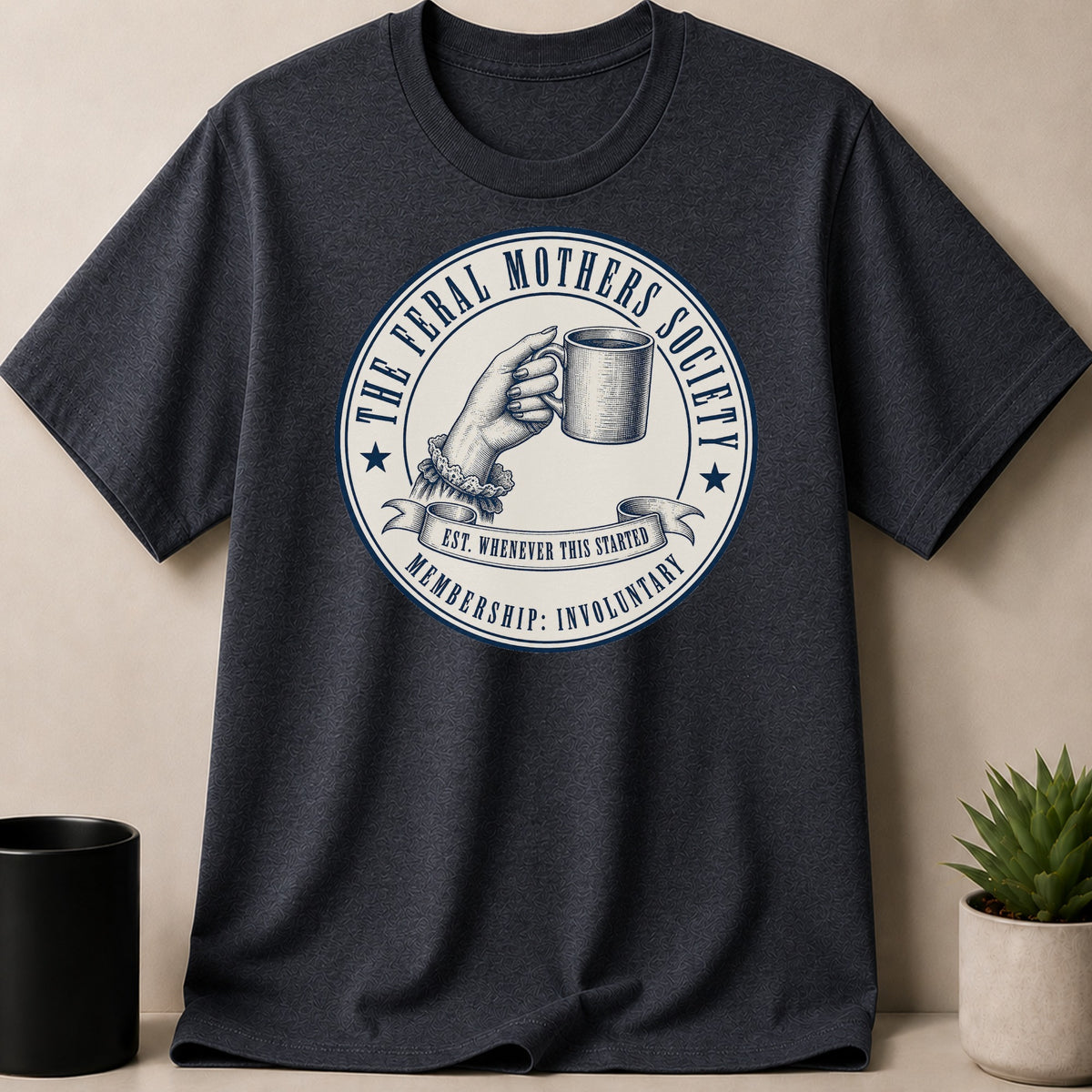 Dark t-shirt with "The Feral Mothers Society" emblem featuring a hand holding a mug.