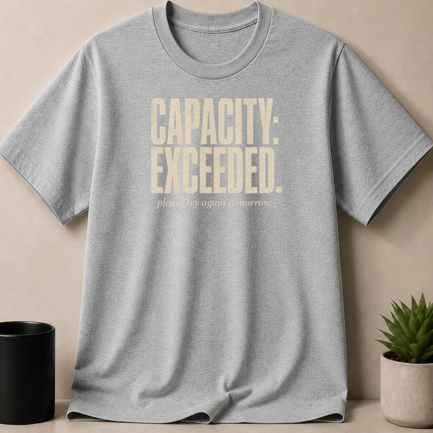 Grey t-shirt with "CAPACITY: EXCEEDED. please try again tomorrow." text.
