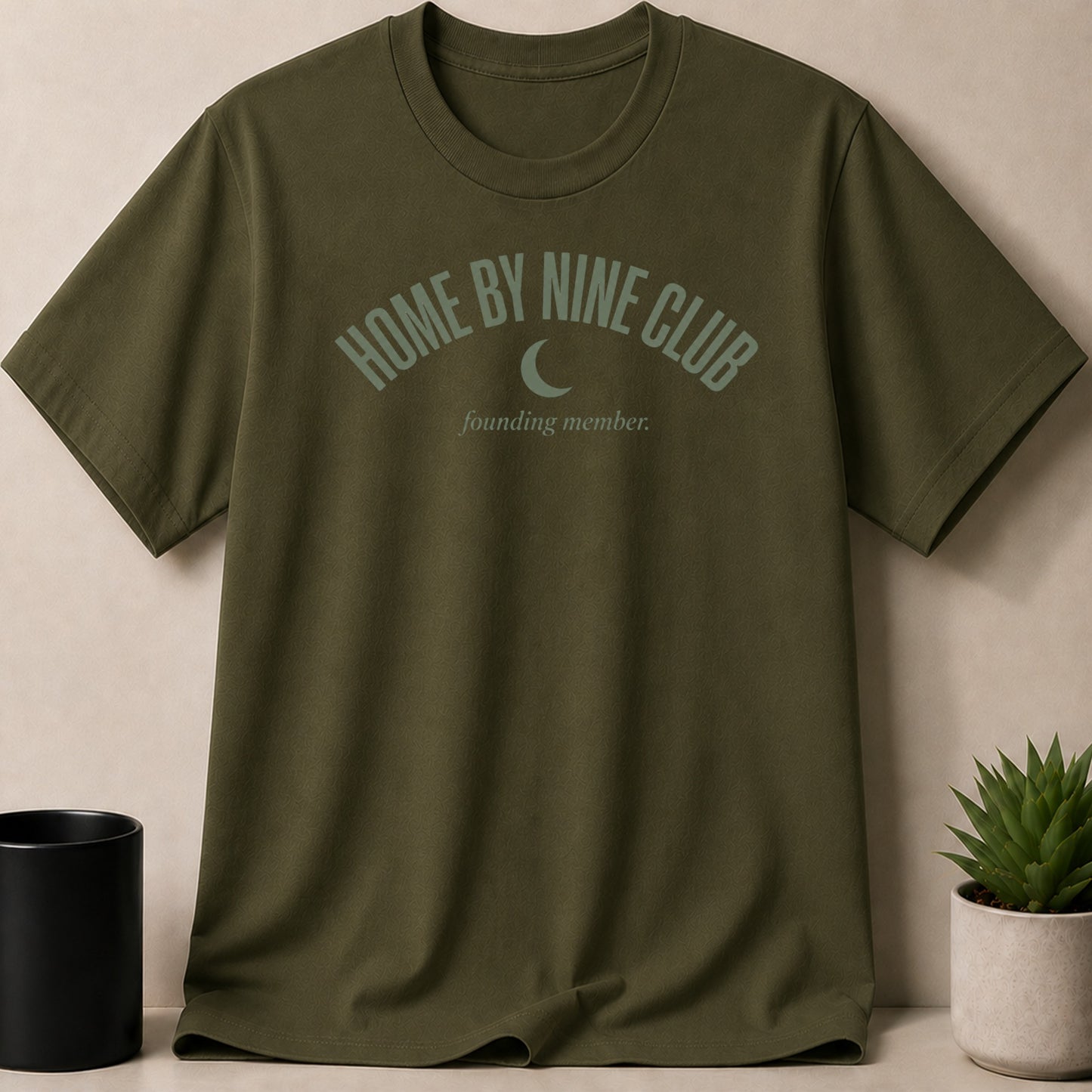 Olive green t-shirt with text "HOME BY NINE CLUB founding member." and a moon graphic.