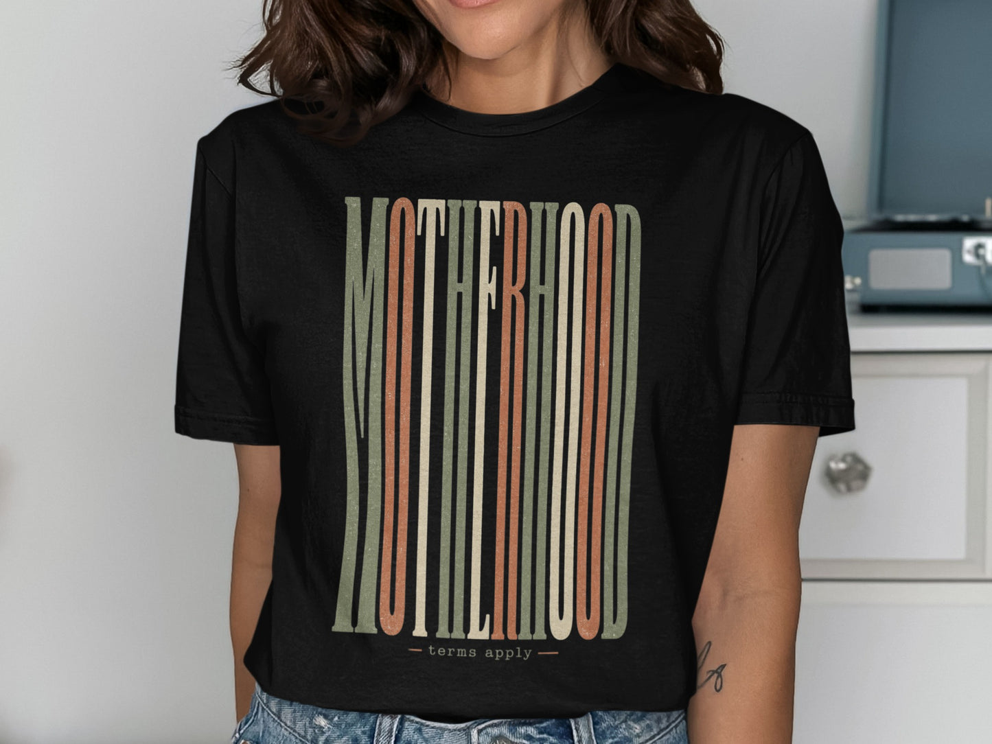 Black t-shirt features "MOTHERHOOD" in vertical, colorful stripes with "terms apply."