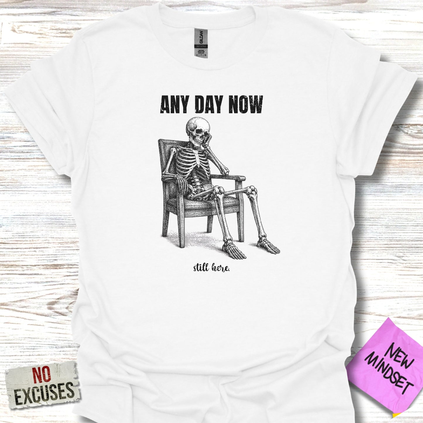 White t-shirt with skeleton sitting in chair, "ANY DAY NOW" and "still here" text.