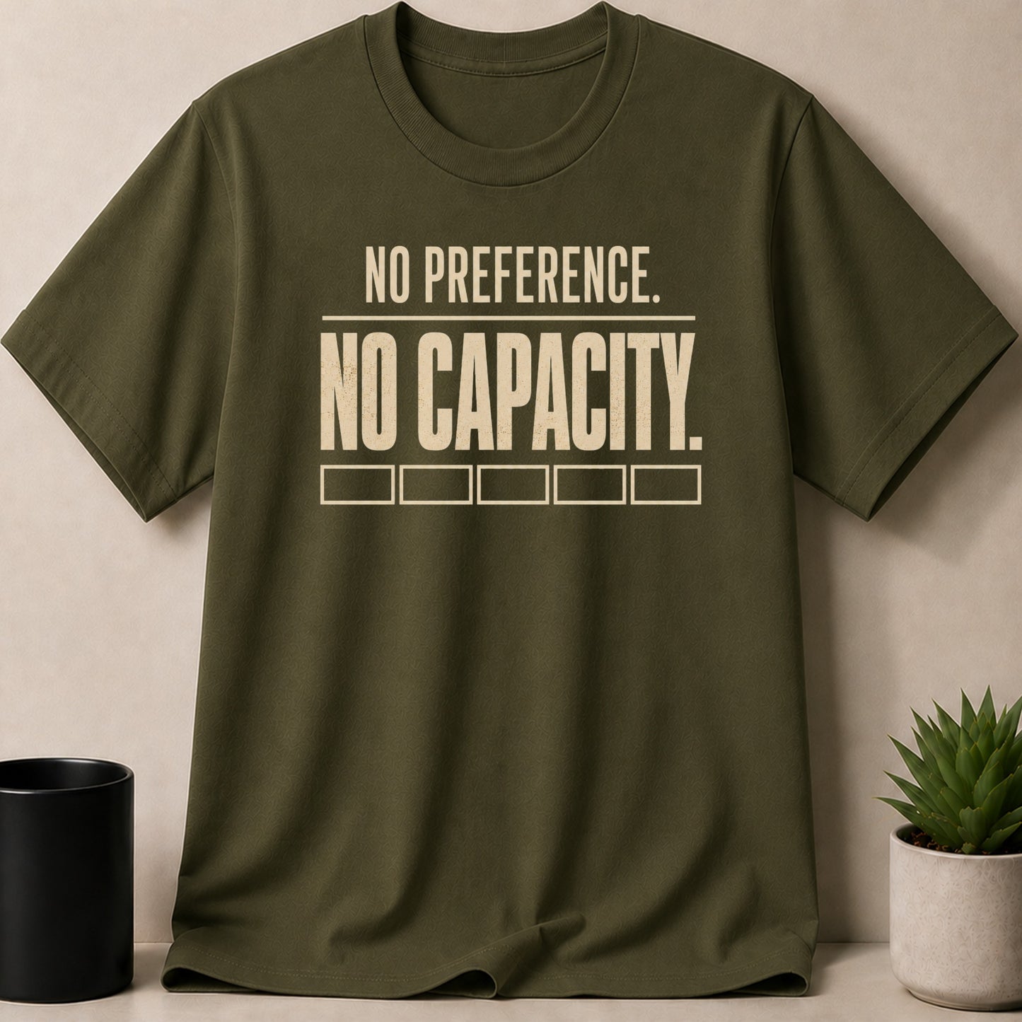 Olive green t-shirt with text "NO PREFERENCE. NO CAPACITY." and five empty boxes.