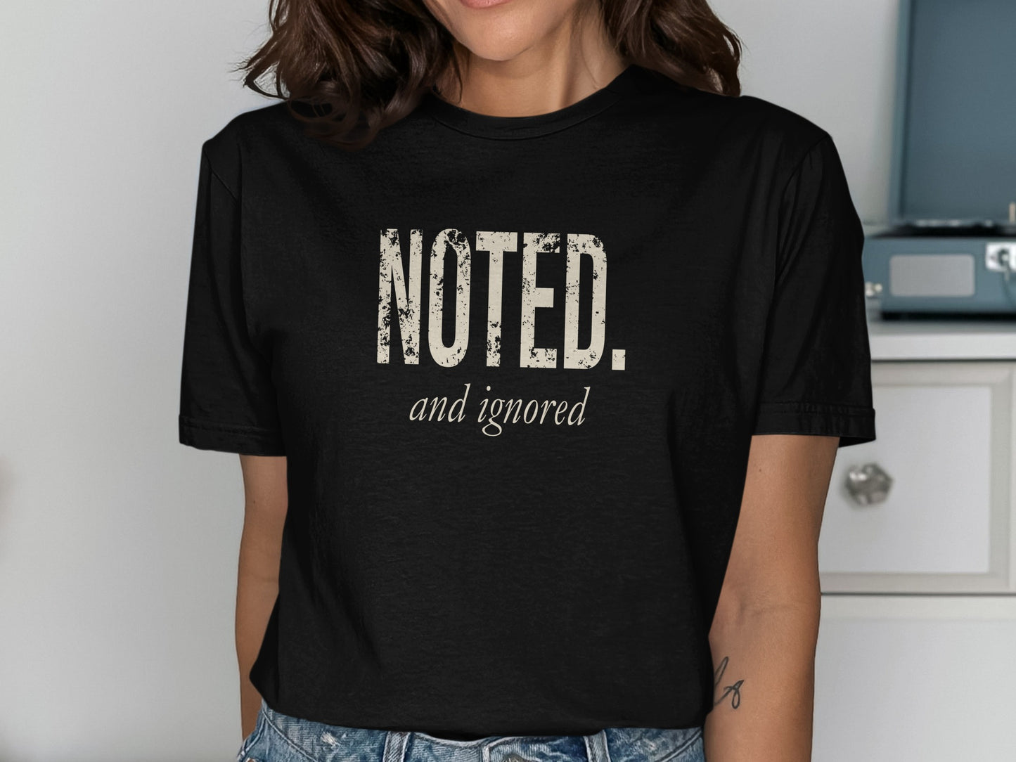 Black t-shirt with distressed "NOTED. and ignored" text in cream.