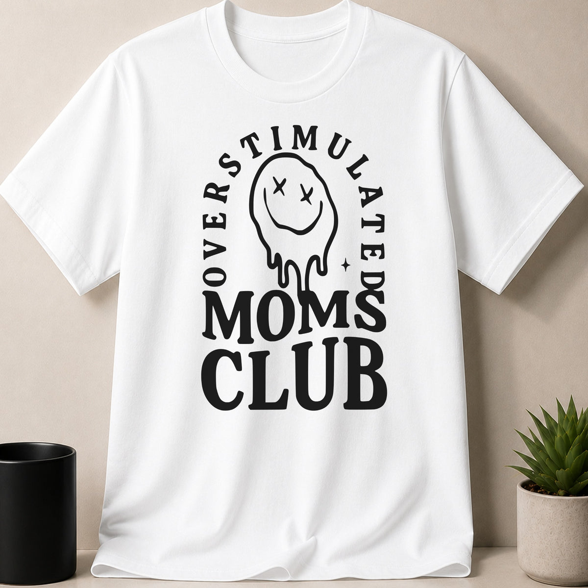 White t-shirt with black text and a dripping smiley face reading "Overstimulated Moms Club".