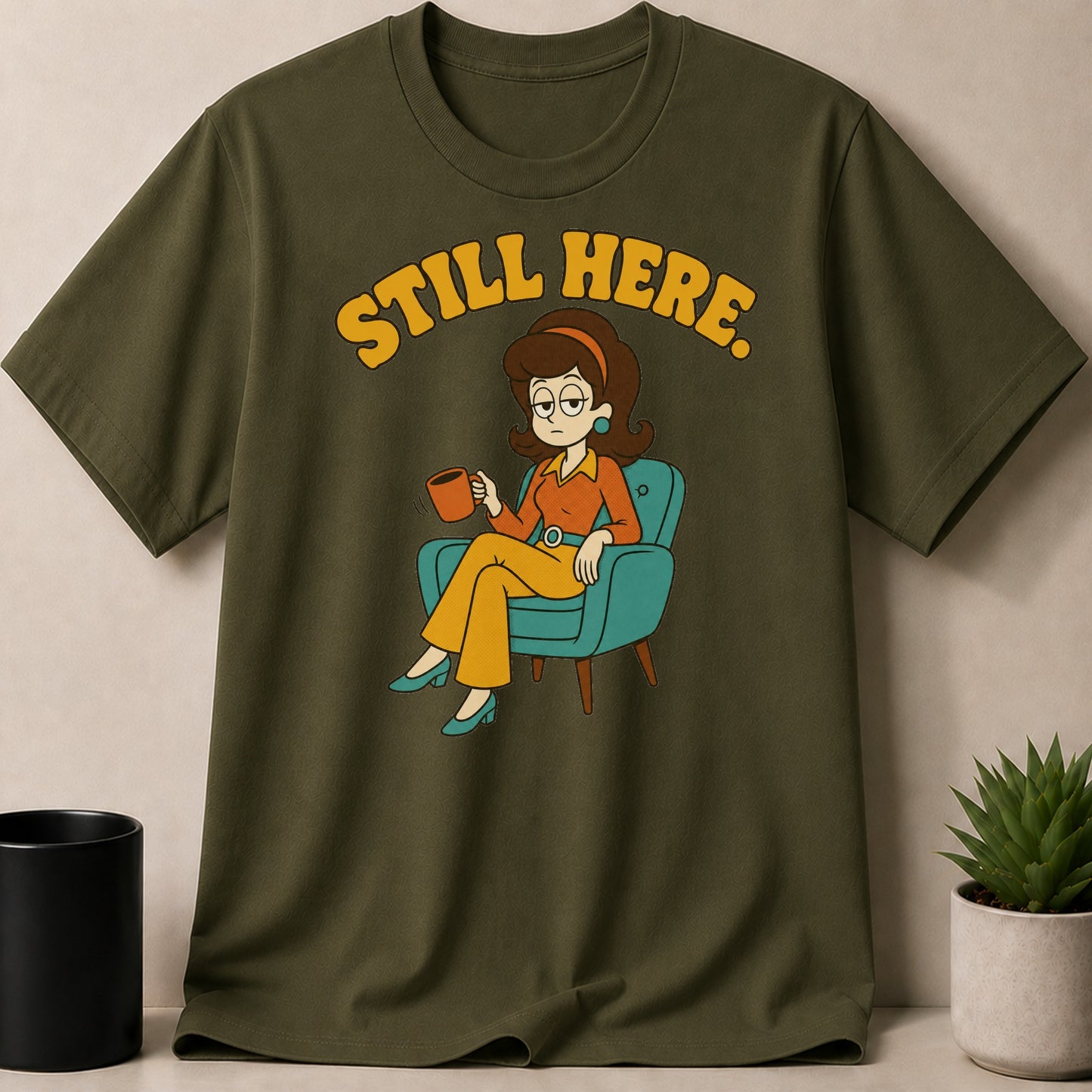 Military Green t-shirt — T-shirt with "STILL HERE." text and cartoon woman sitting in a chair with a mug.