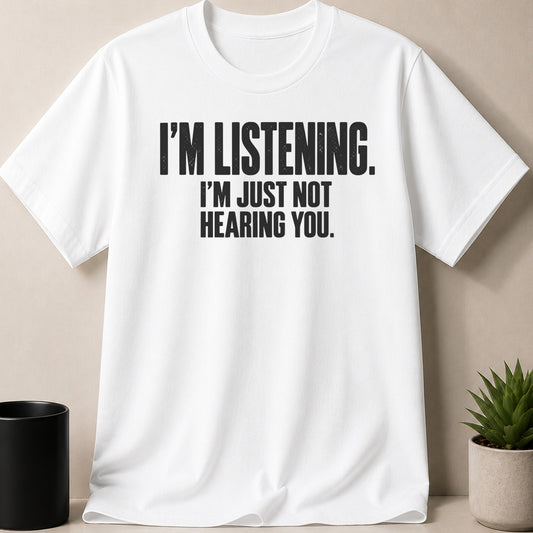 A white crewneck t-shirt features bold black text reading "I'M LISTENING. I'M JUST NOT HEARING YOU."