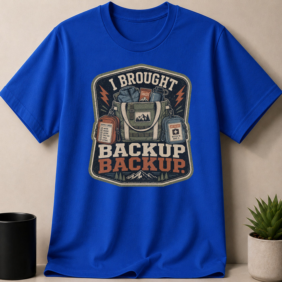Blue t-shirt graphic with text "I BROUGHT BACKUP BACKUP" and camping gear.