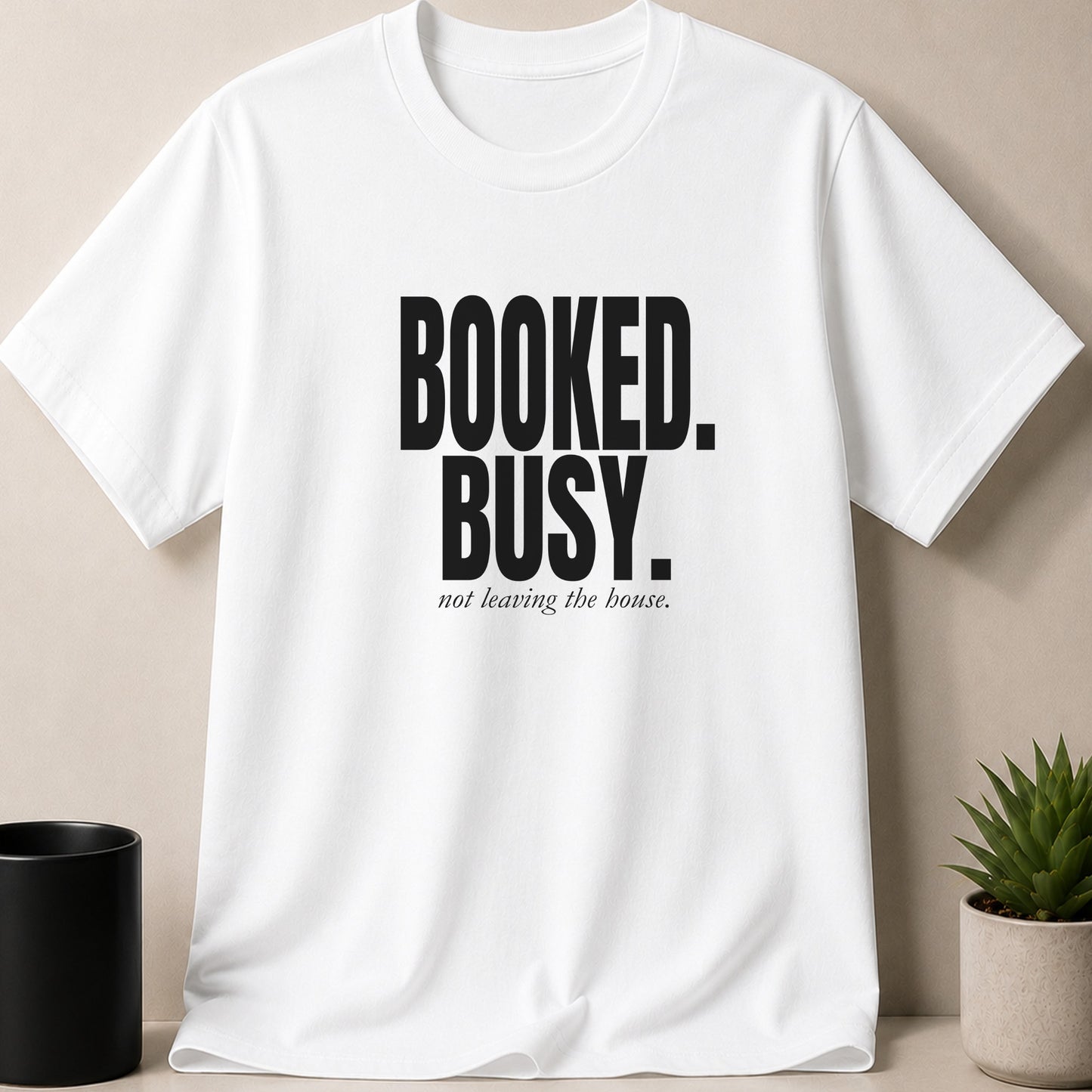 White t-shirt with black text "BOOKED. BUSY. not leaving the house."