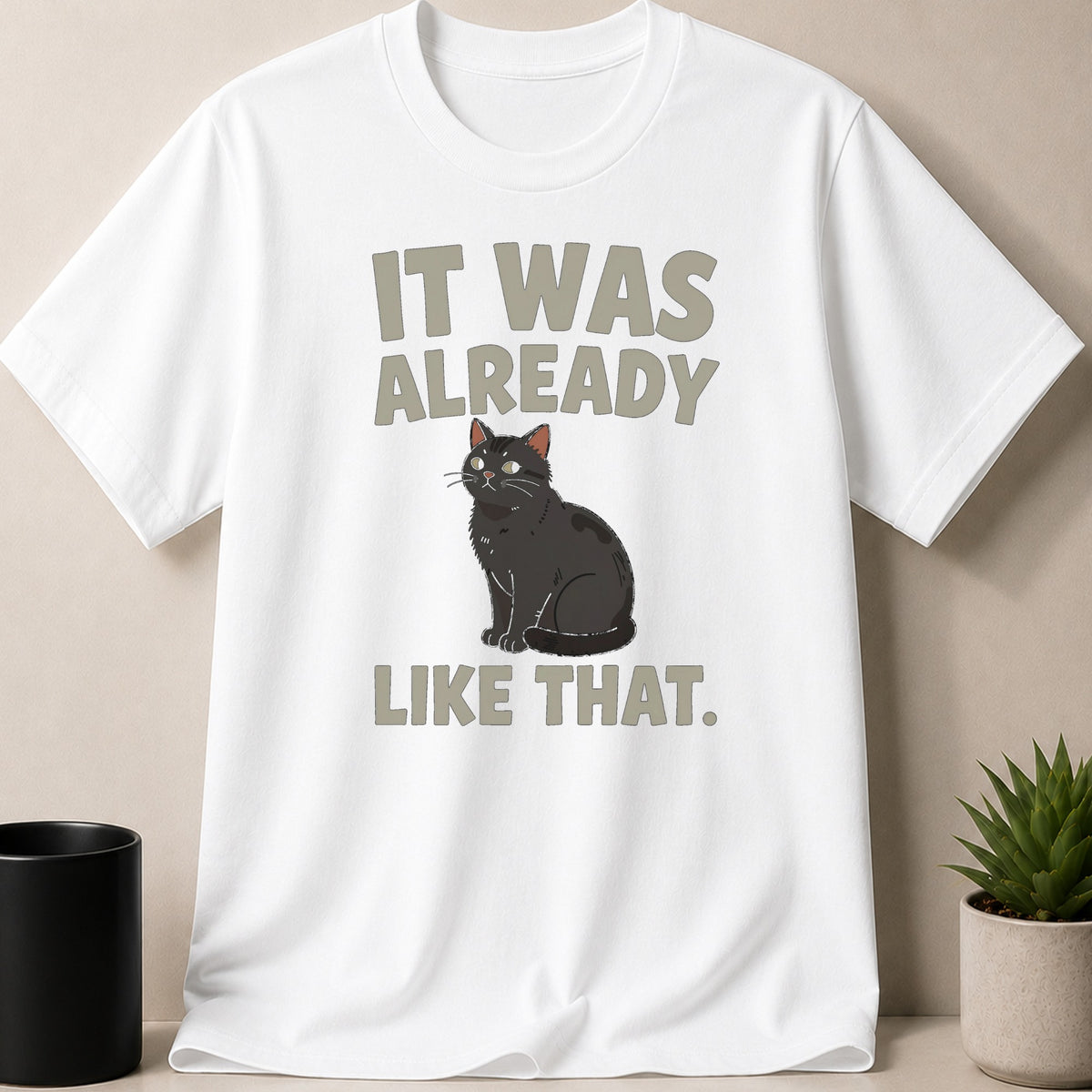 A white t-shirt featuring a cartoon black cat illustration and gray text reading "It was already like that."