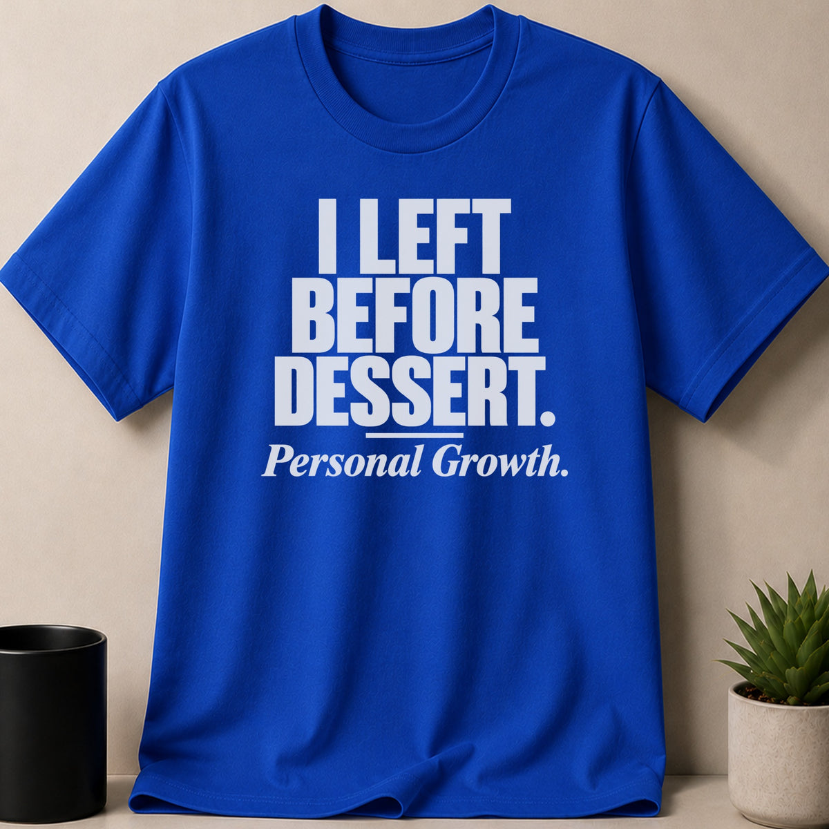 A blue crewneck t-shirt with white text that reads I LEFT BEFORE DESSERT and Personal Growth.