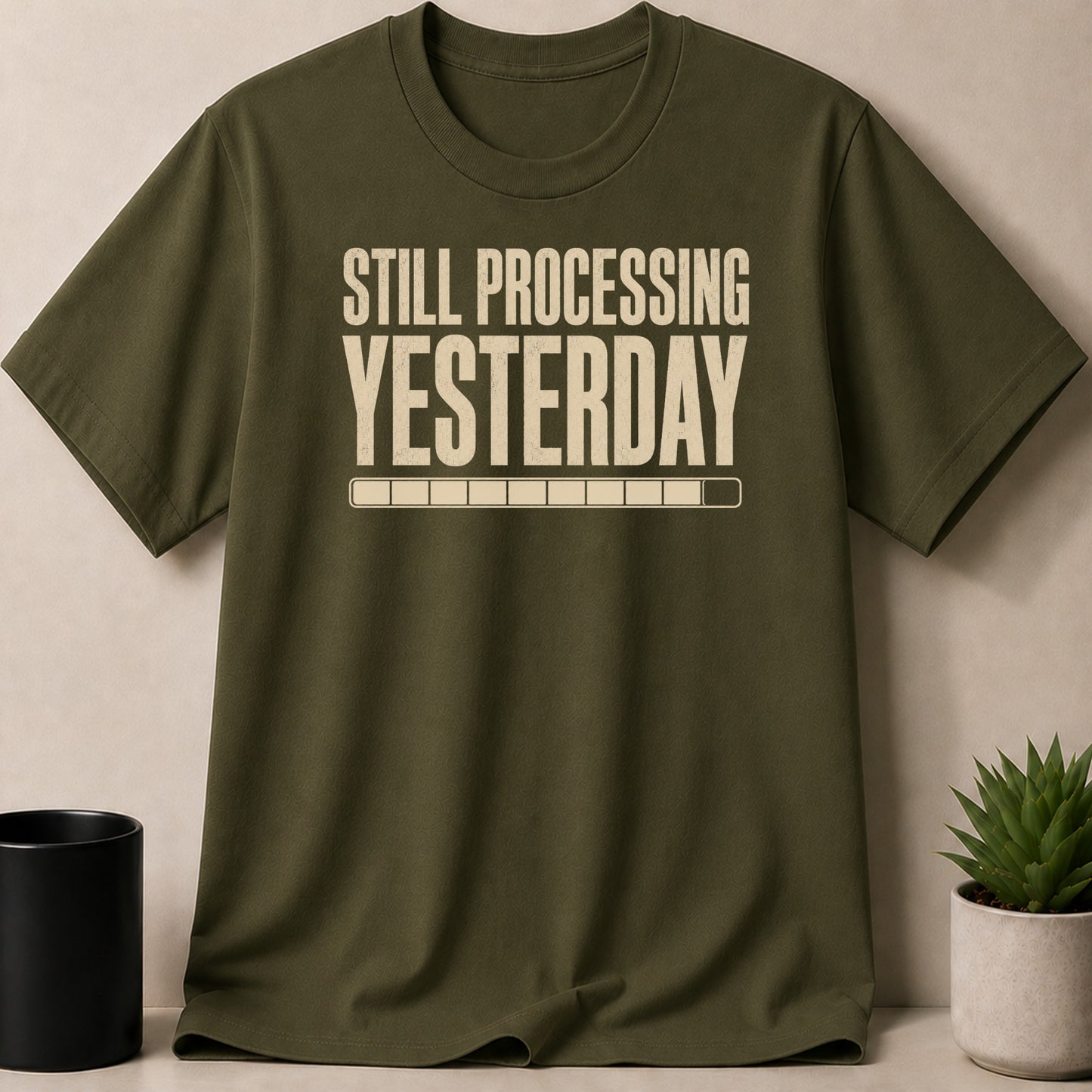 Olive green t-shirt with "STILL PROCESSING YESTERDAY" text and a progress bar.