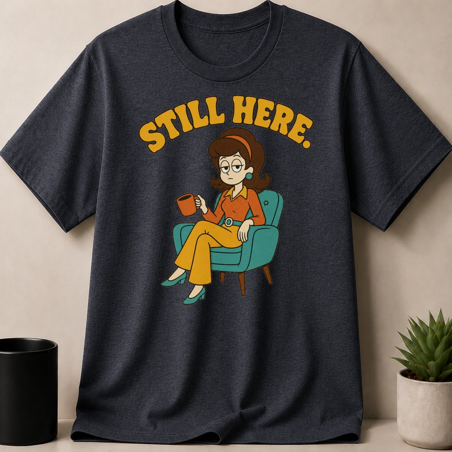 Dark t-shirt with cartoon woman sitting and holding coffee cup, text "STILL HERE."
