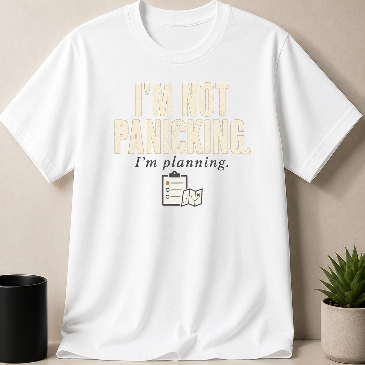 White t-shirt with "I'm Not Panicking. I'm Planning." and clipboard with map icons.