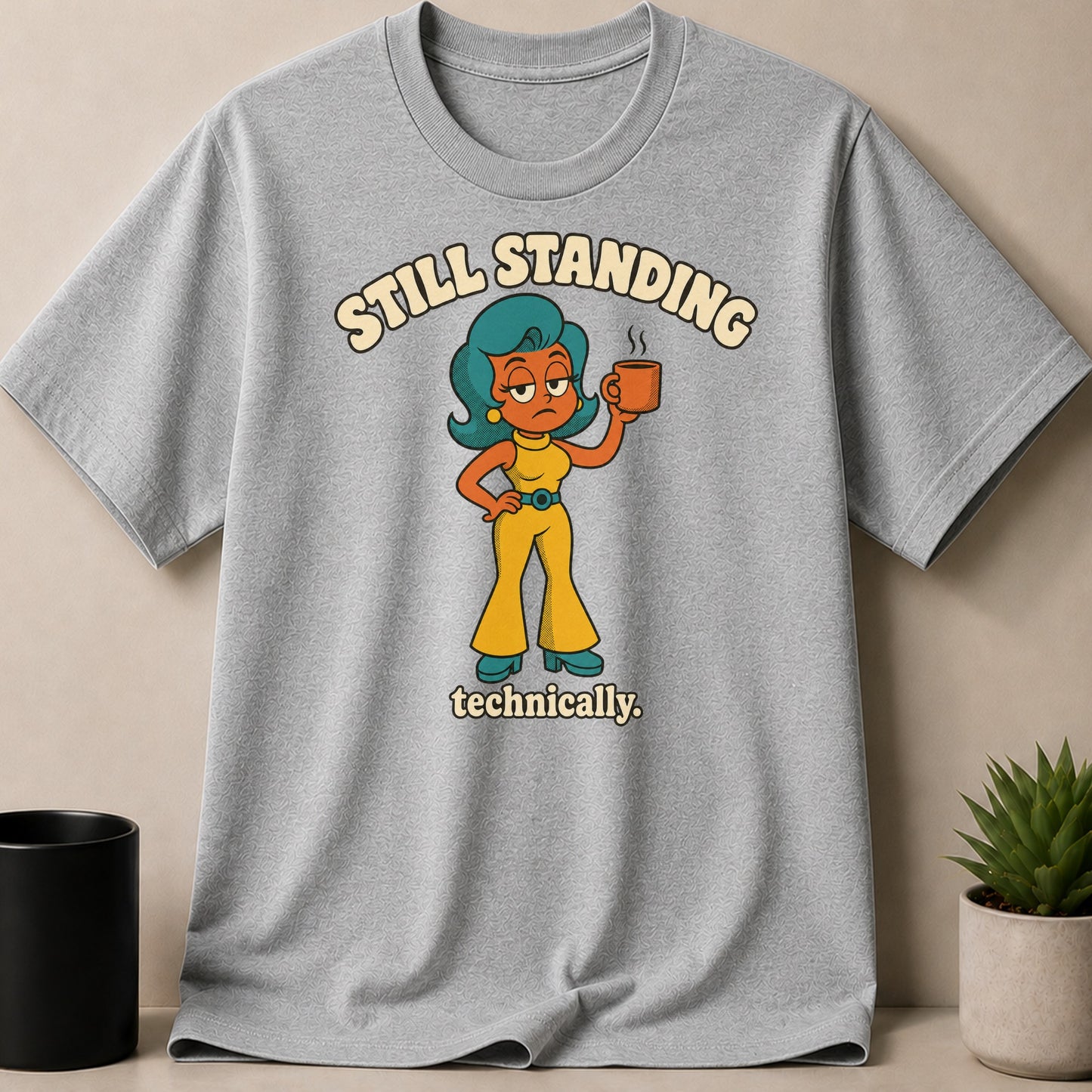 Grey t-shirt with cartoon woman holding coffee mug and text "STILL STANDING technically."
