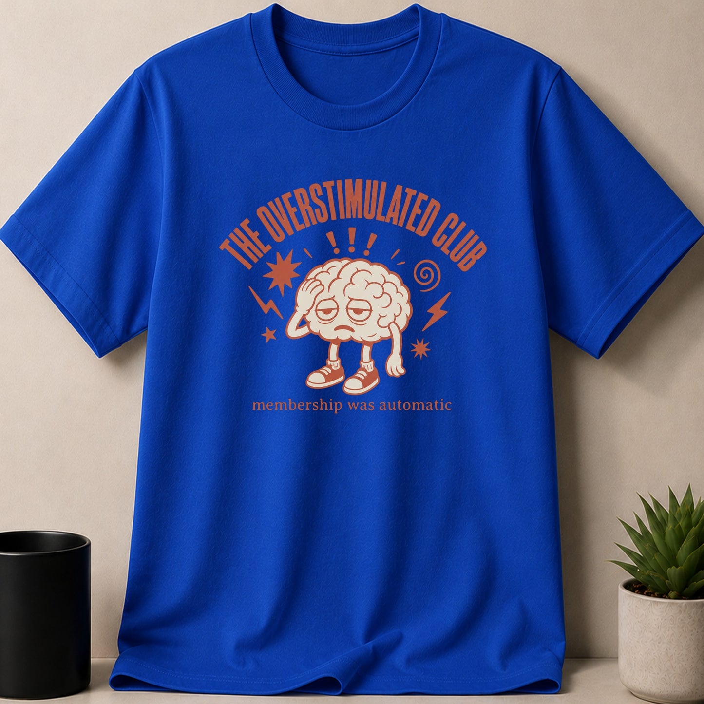 Blue t-shirt with "The Overstimulated Club" text and a tired brain graphic.