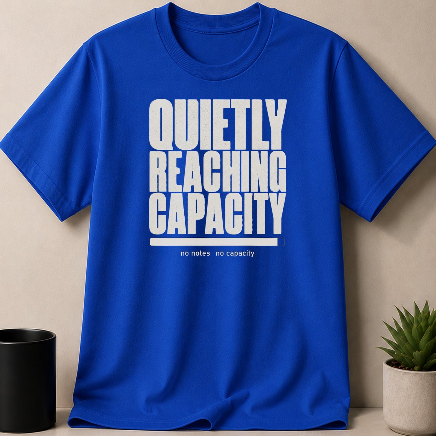 Blue t-shirt with white text "QUIETLY REACHING CAPACITY" and a progress bar.