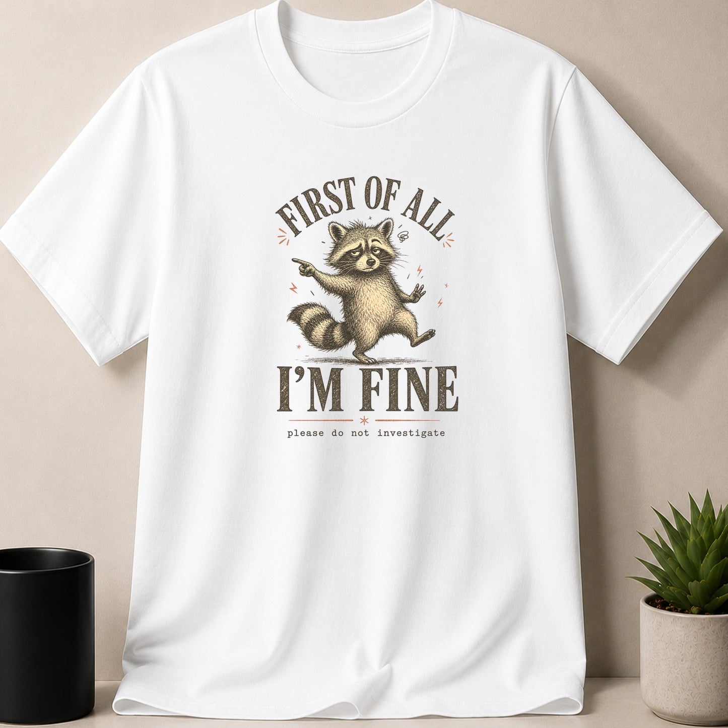 White t-shirt with a raccoon graphic and text: "FIRST OF ALL I'M FINE please do not investigate".