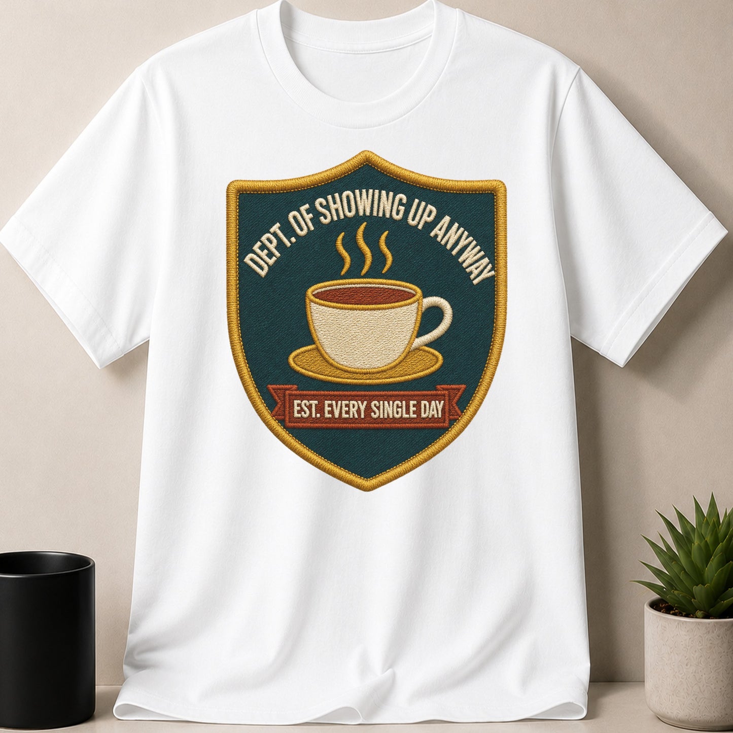 White t-shirt with embroidered shield logo featuring a coffee cup and "Dept. Of Showing Up Anyway Est. Every Single Day."