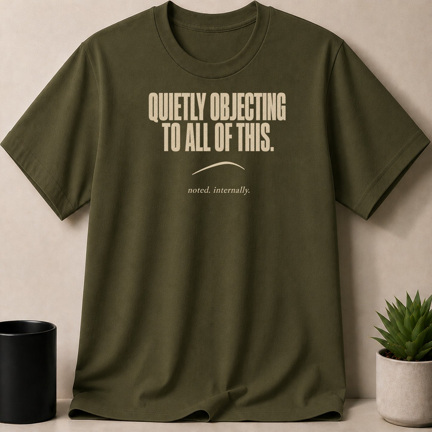 Olive green t-shirt with text "QUIETLY OBJECTING TO ALL OF THIS. noted. internally."
