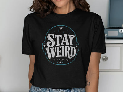 Black t-shirt with blue and white "STAY WEIRD it's working" graphic.