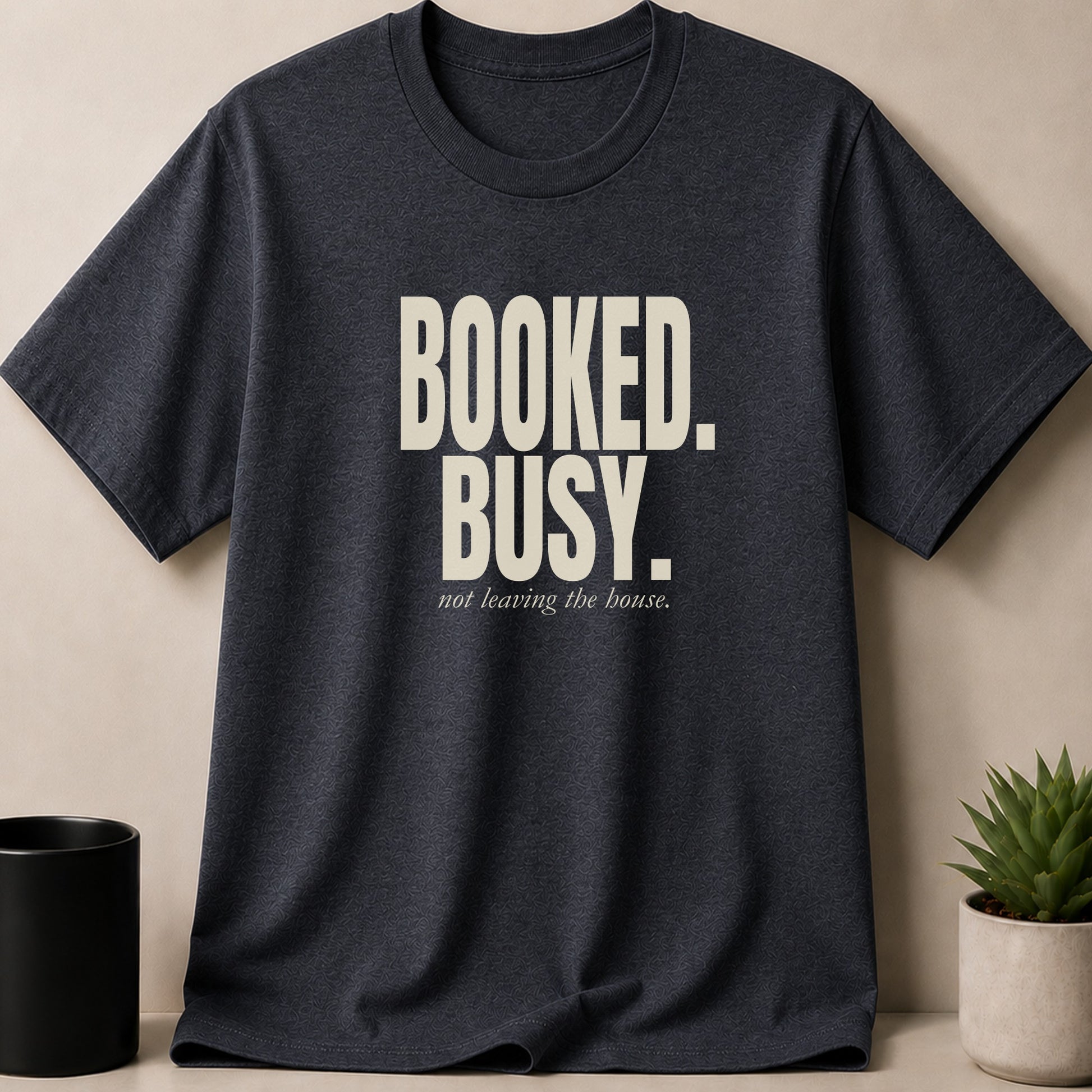 Dark grey t-shirt with cream text reading "Booked. Busy. not leaving the house."