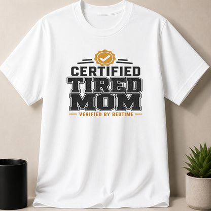White t-shirt with "Certified Tired Mom Verified by Bedtime" graphic and a gold check mark badge.